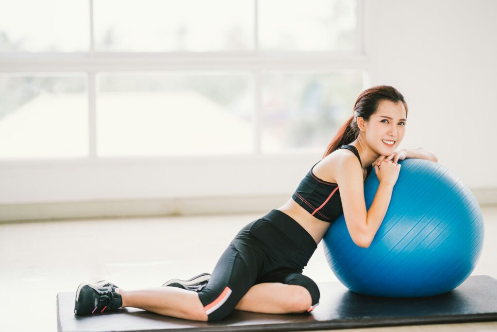 Happy young Asian woman health exercise alone at home gym or sports club, rest on fitness ball