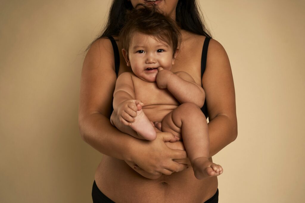 Portrait of cheerful Asian toddler carried by unrecognizable mother